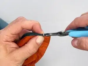 Com um alicate, dobre as garras do tope para dentro, apertando-as ao redor do espiral do zíper. As garras irão agarrar no espiral, fixando-o no lugar.