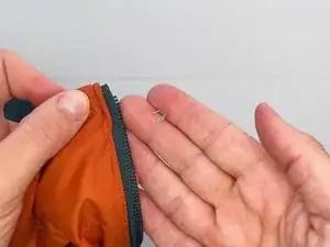 Posicione o tope superior no lado achatado da fita do zíper, alinhando o lado com a garra dupla do tope, de modo que ele fique virado para a jaqueta e o lado com a garra única esteja virado para os dentes do zíper.