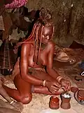 Mulher himba preparando um desodorante à base de ervas aromáticas e resina vegetal. O desodorante será queimado e a fumaça aplicada sobre o corpo, aromatizando-o.