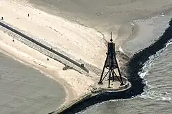 Vista aérea da Kugelbake em Cuxhaven, Alemanha, mostrando a estrutura de madeira erguida sobre uma faixa de areia durante a maré baixa.
