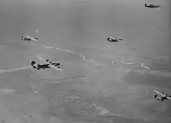 Formação de B-24 em missão a Bucareste em 1944. Note o bombardeiro danificado com o motor fumegante.
