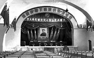 Local em que foi realizado o o 7º Congresso Nacional do Partido Comunista da China. Ao centro do auditório, um retrato imenso de Mao Zedong. Ao lado direito do auditório, retratos de Karl Marx e Friedrich Engels