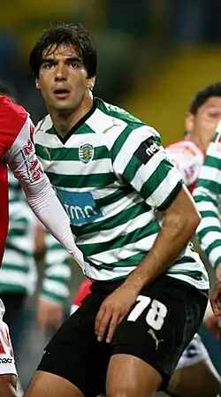 Um homem com uniforme de futebol e olhando para longe da câmera, com cara de concentrado, posicionando-se para a chegada da bola.