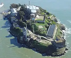 A young man sitting down, wearing a striped shirt. Behind him, three men wearing the same shirt and dark shorts are partially visible