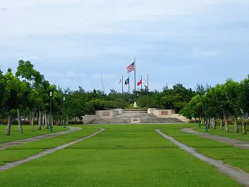 Fotografia em perspectiva do parque, que se eleva por uma ampla escadaria que termina em um pátio e um círculo de cinco bandeiras.