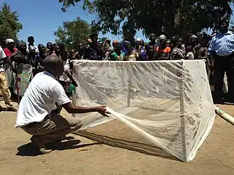 Reunião na comunidade do Dombe, promovida pela "Iniciativa do Presidente contra a Malária" (programa do governo dos Estados Unidos), em 2015, onde é apresentado e explicado sobre o uso de mosquiteiros de modo a evitar doenças tropicais.