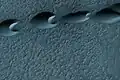 Barcanas na região de Hellespontus, visto pela HiRISE. Os "chifres" apontam para baixo, conclui-se daí que os ventos que formaram as dunas vieram do oeste.
