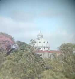 Mesmo distante, a enorme cúpula da igreja se destaca entre algumas árvores.