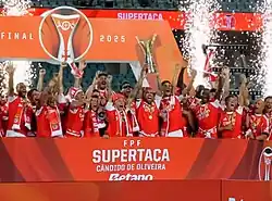 Uma equipe comemorando a conquista de um campeonato, com o capitão erguendo a taça.
