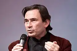 Photograph of a middle-aged man speaking into a microphone.