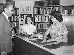 Bibliotecárias conversam com homem, enquanto organizam livros e documentos