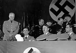 Imagem de uma reunião da cúpula nazista, em outubro de 1936. Philipp Bouhler esta a esquerda de Hitler (sentado, na direita da imagem). Joseph Goebbels esta sentado na outra ponta.