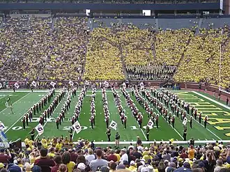 imagem retrata jogo de futebol americano em um estádio lotado; há uma banda marcial tocando
