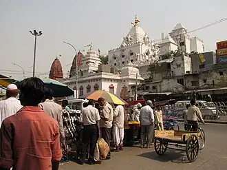 Extremidade oriental da Chandni Chowk. O edifício branco é o Gauri Shankar Mandir, um emplo hindu dedicado a Xiva. À esquerda avistam-se as torres vermelhas do Digambara Mandir, o templo jainista mais antigo de Deli.