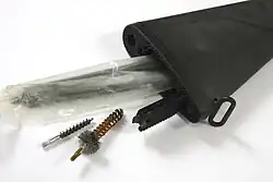 Compartimento de armazenamento dentro da coronha com alçapão aberto.