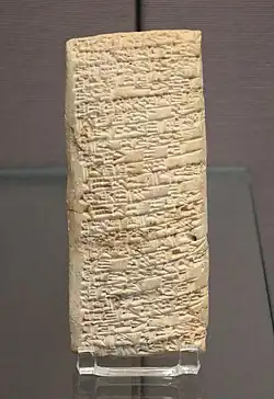 A long, rectangular tablet of sand-coloured clay, inscribed all over with cuneiform text.