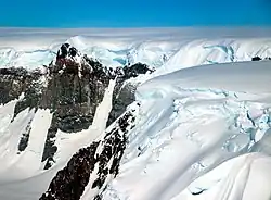 Grande escarpa de montanha rochosa coberta em um dos lados até sua altura máxima por uma enorme extensão de geleira.