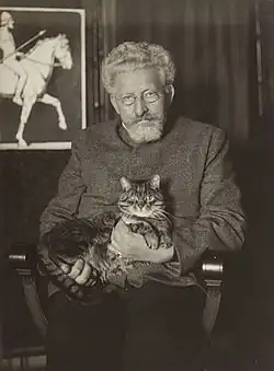Michael Georg Conrad já de cabelos grisalhos, com um gato no colo, em seu apartamento. Fotografia sem data.