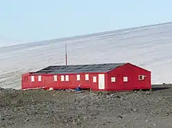 Estação Científica Antártica Ruperto Elichiribehety, estrutura vermelha em meio ao gelo e rochas da Antártida.