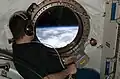 Astronauta observa a Terra através da escotilha do módulo Kibo.