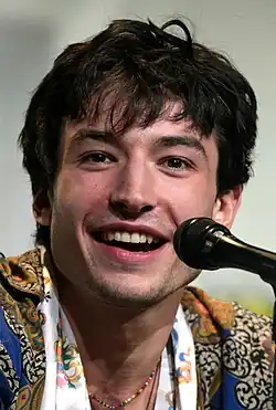 Uma fotografia de Ezra Miller falando em uma convenção atrás de um microfone