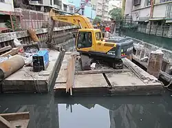 uma retroescavadeira operando sobre uma placa flutuante em um canal urbano