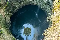 vista de cima de uma grande cratera em formato de poço contendo um lago no fundo.