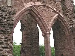 Parte de um castelo, com um enorme arco semicircular contendo dois pequenos arcos normandos dominando a imagem. Através dos arcos, uma coluna em ruínas pode ser apenas vista.