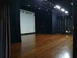 Interior do Teatro Laboratório - TELAB, no campus Curitiba II. Na imagem vemos um palco, o urdimento, cortinas, e piso de madeira.