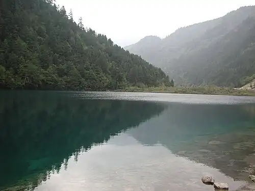 Vale Jiuzhaigou envolto em névoa matinal, com reflexos nos lagos