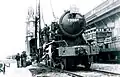 A antiga locomotiva a vapor WD Austerity 2-8-0 do Exército Britânico chegando em Hong Kong em 1947 para a secção britânica do Caminho de Ferro de Kowloon-Cantão. A Torre do Relógio pode ser vista no fundo.