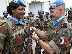 Uma boina azul beninense, armada com um fuzil PM md. 63, é condecorada por um general francês.