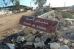 Placa suja dizendo "Prison of Khiam" em cima de escombros.
