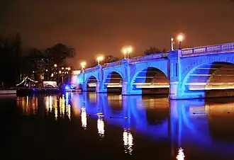 Foto de uma ponte rodoviária que atravessa o rio à noite, iluminada com luzes azuis.
