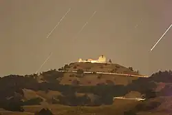 Fotografia em time-lapse de edifícios brancos no topo de uma montanha à noite com estrelas riscando o céu.