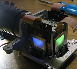 Parte do conjunto ótico de um projetor LCD. À mostra os painéis LCD e lente objetiva (à esquerda).