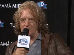 Um homem de meia idade com cabelo loiro comprido e encaracolado falando ao microfone.