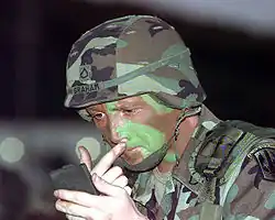Foto de um soldado aplicando tinta de camuflagem no rosto