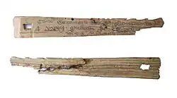 Duas pequenas peças de madeira, ligeiramente triangulares; estas são duas metades da mesma peça. A peça superior mostra escrita em inglês antigo; a inferior é mais rugosa.