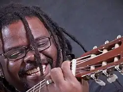 Mestre Jonas com cabelo trançado tocando violão