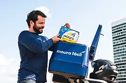 Homem com roupa azul segurando uma bateria aotomotiva das mãoes