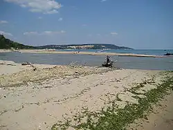 Imagem aérea mostrando a foz do rio Kamchia desembocando no mar Negro, com formação de cordão arenoso separando a água fluvial da marinha.