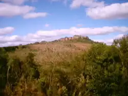 paisagem com colina no fundo, contendo formações rochosas semelhantes a antigas estruturas arquitetônicas.