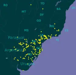 Mapa mostrando a distribuição geográfica confirmada de M. coccinea em pontos amarelos.