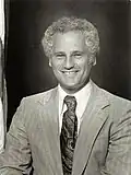 Black-and-white photo of a man with a wide smile and short curly hair wearing a light-colored suit