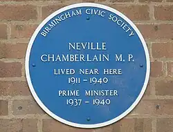 Placa azul redonda em uma parede de tijolos. Diz "BIRMINGHAM CIVIC SOCIETY", "NEVILLE CHAMBERLAIN M.P.", "LIVED NEAR HERE 1911–1940", "PRIME MINISTER 1937–1940".