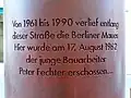 Texto inscrito no monumento. Em português: de 1961 a 1990 ao longo desta estrada correu o Muro de Berlim. Aqui o jovem operário Peter Fechter foi baleado em 17 de agosto de 1962...