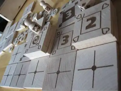 A imagem mostra um conjunto do jogo Piecepack feito de madeira, na imagem há uma série de lajotas divididas em forma de cruz, utilizadas como parte do tabuleiro.