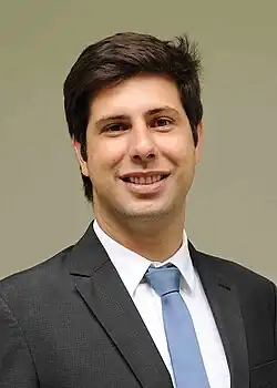 Rafael Picciani sorrindo e vestindo um terno com gravata azul.