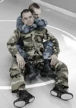 Em um campo, um militar está fazendo o Mata-Leão.